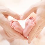 Tiny Newborn Baby's feet on female Heart Shaped hands closeup